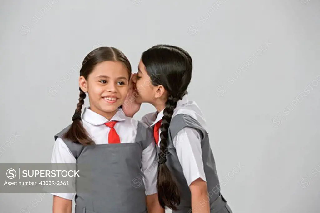 Two girls wearing school uniform telling secrets to each other