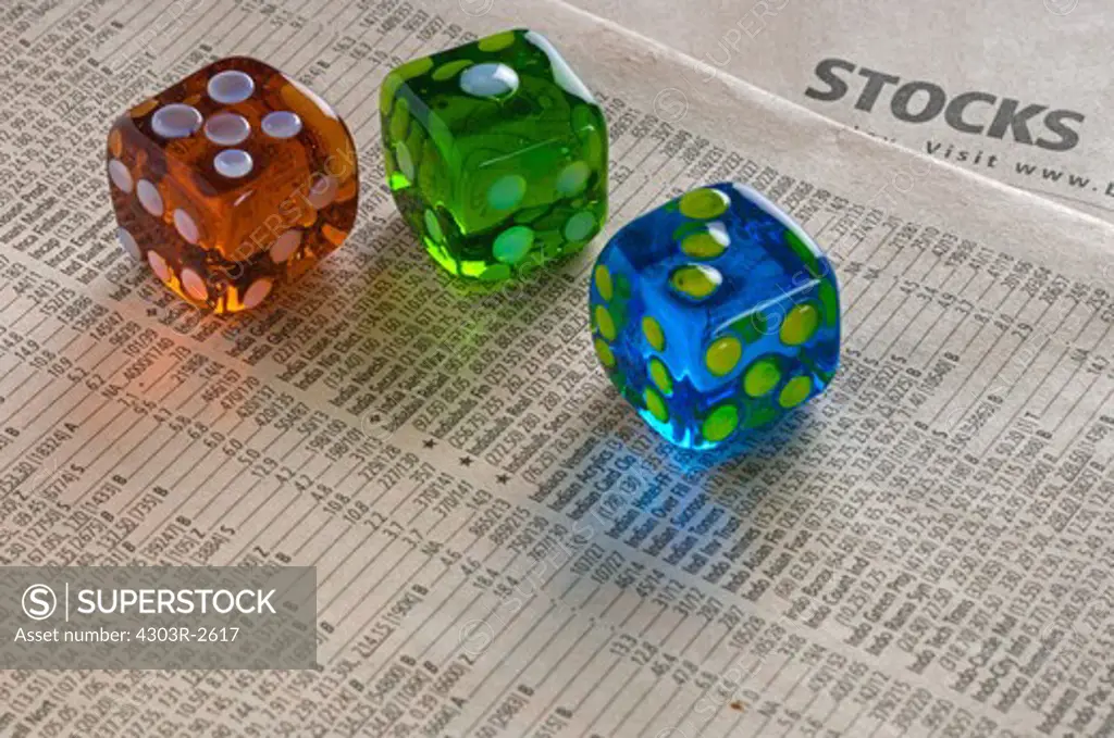 Three colorful dice on top of a newspapers stockmarket pages