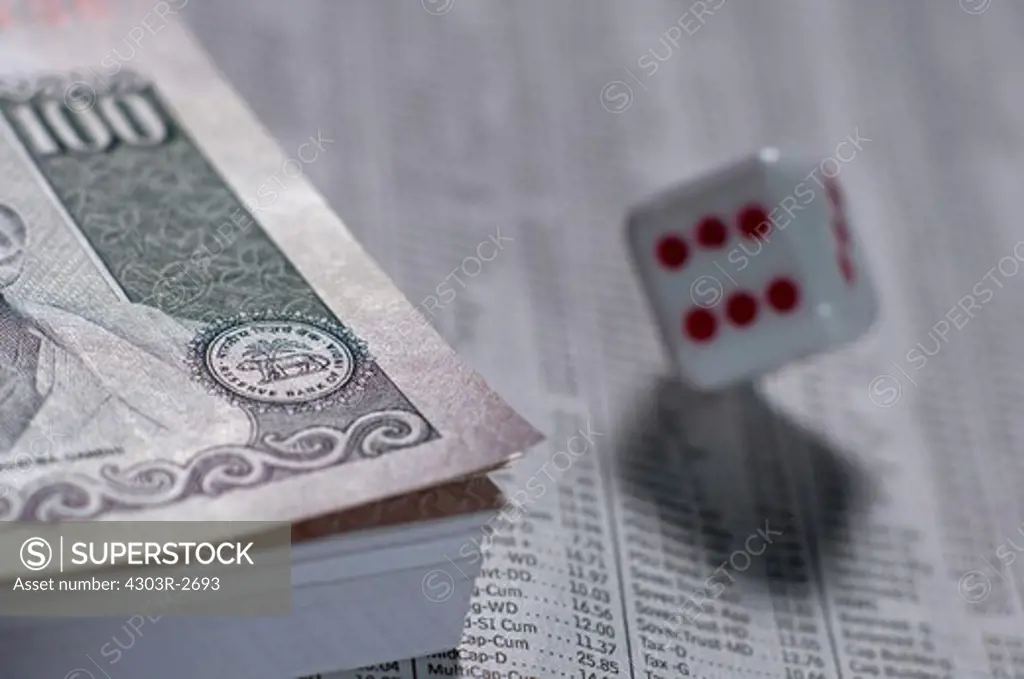Bundle of indian rupee banknotes with a dice on top of business section a newspaper