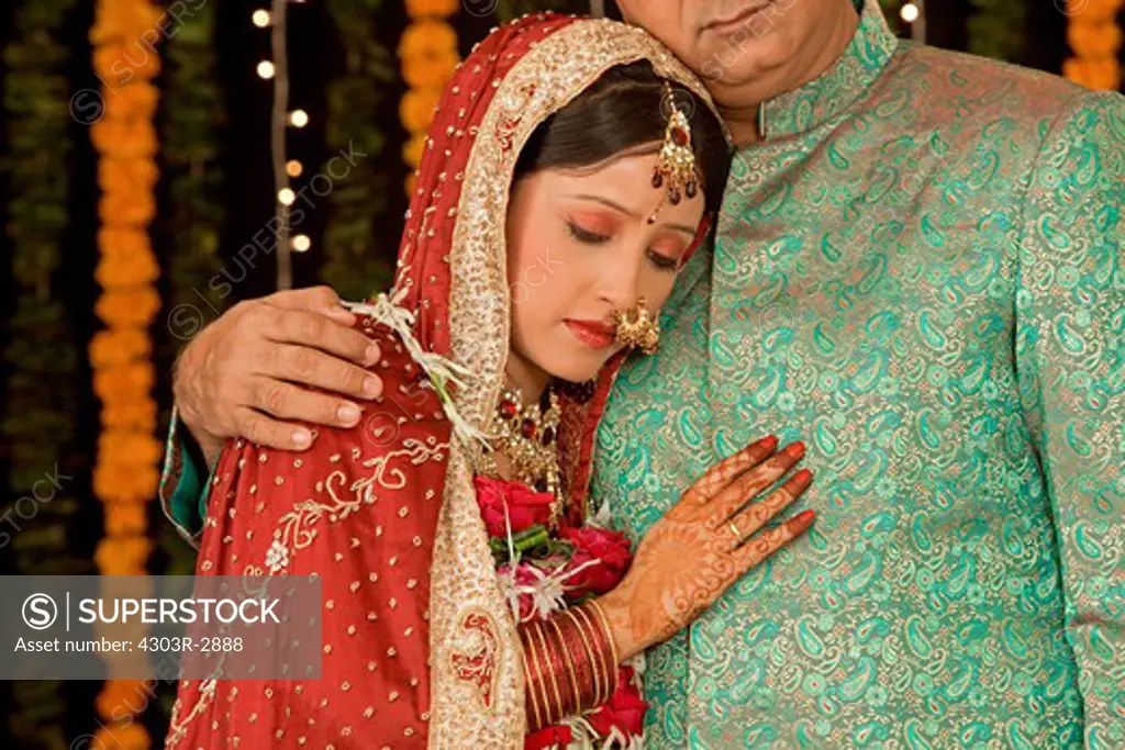 Sad indian father hugging her daughter wearing a wedding dress