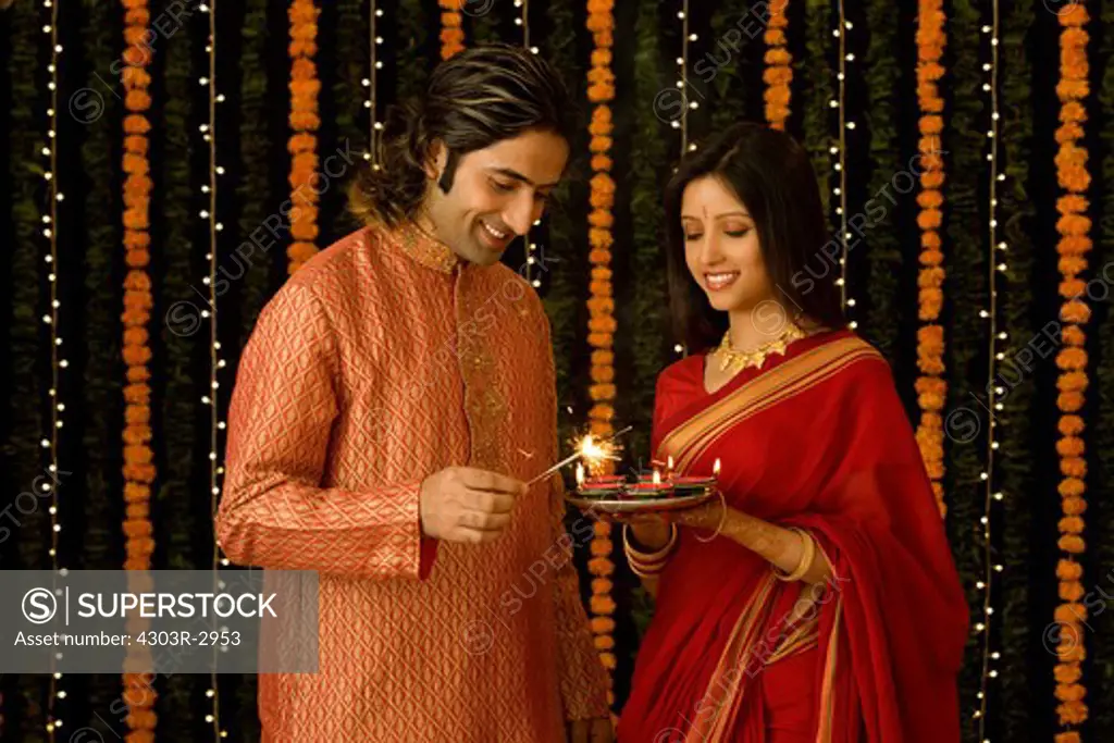 Indian man lighting a small fire work and woman with a plate of candles