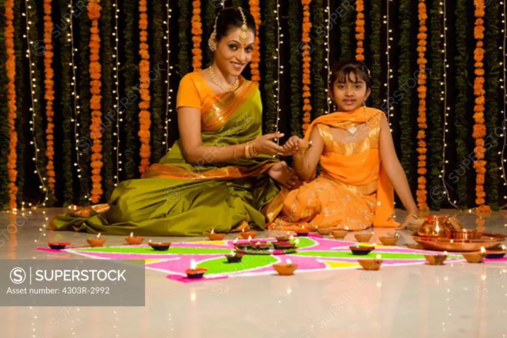 Indian mother and daughter lighting an oil lamp in front of rangoli