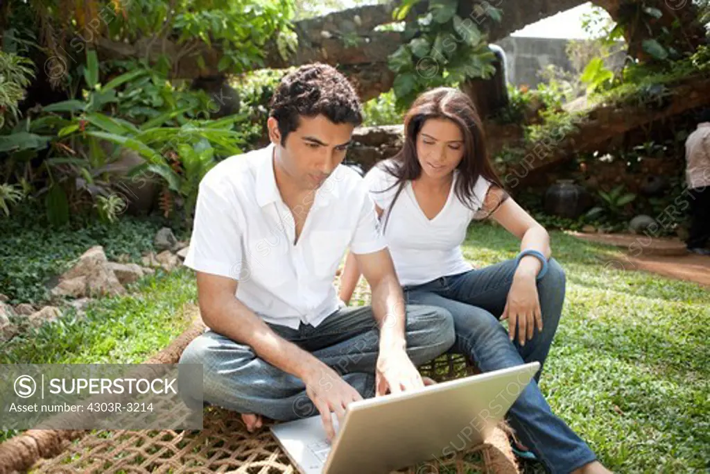 Couple with laptop sitting in the garden