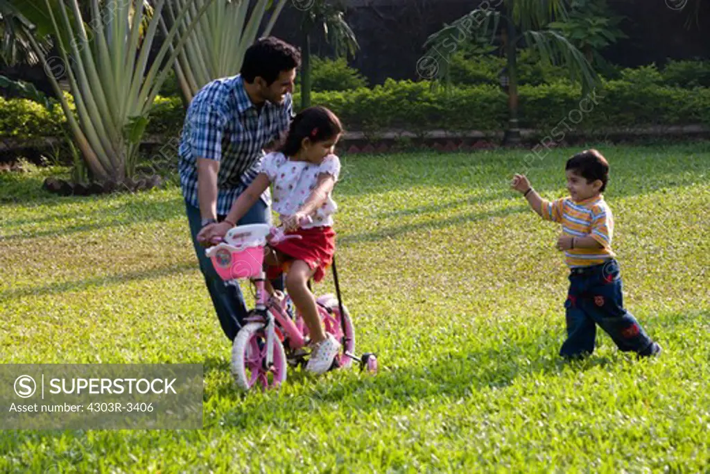 Daughter learning bicycle with her father, son chasing
