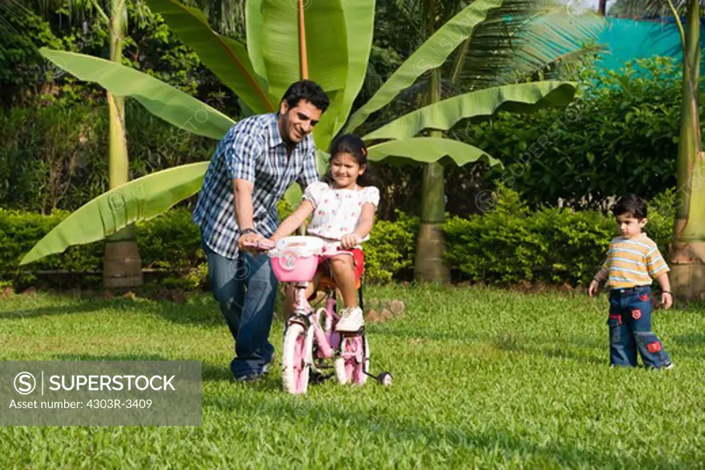 Daughter learning bicycle with her father, son chasing