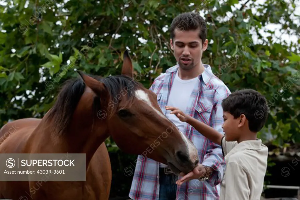 Father and son feeding a horse, smiling.