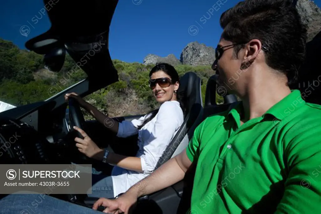 Couple riding in a convertible car, smiling.