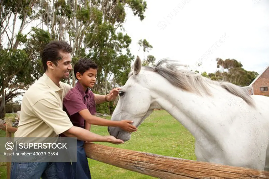 Father and son holding a horse, smiling.
