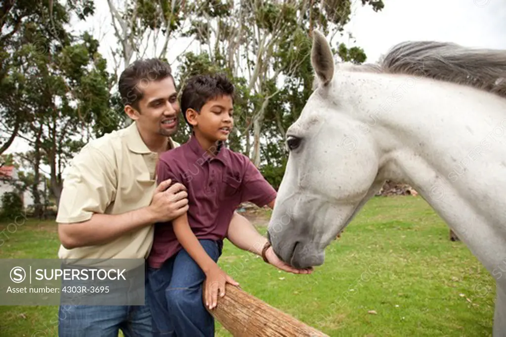 Father and son holding a horse, smiling.