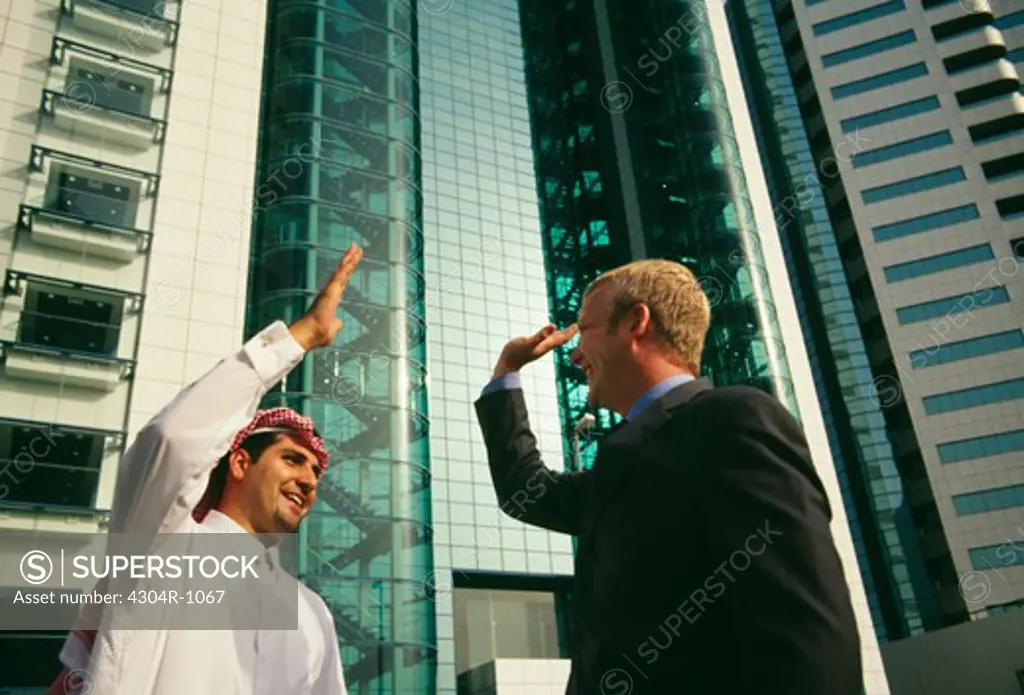 An Arab and a businessman greeting each other happily near a commercial complex