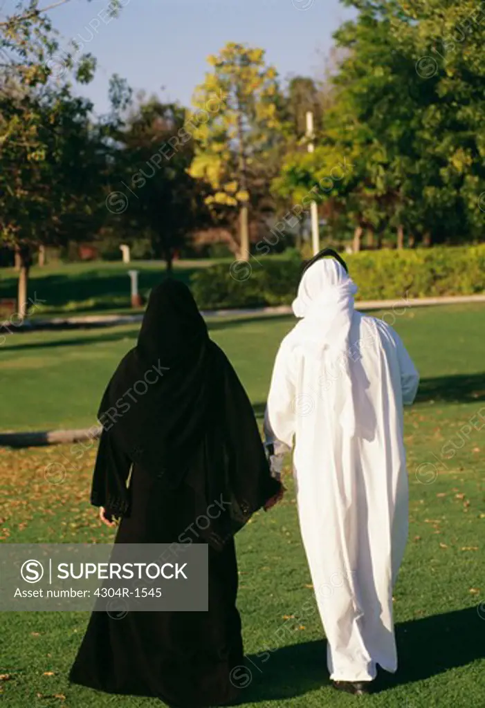 Rear view of an Arab couple hold hands as they take a stroll in the park.