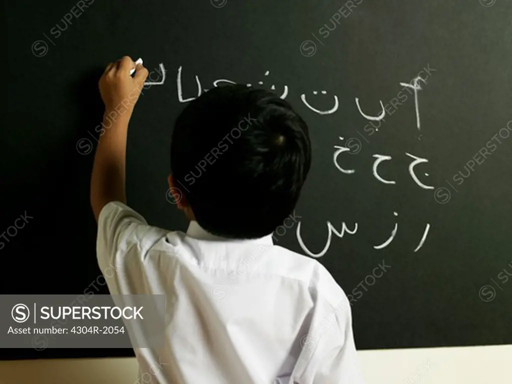 Boy writing Arabic letters on the black board