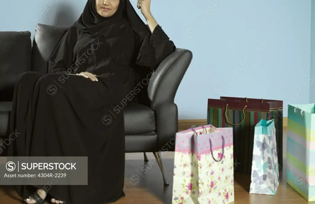 An Arab lady sitting on a sofa with a shopping bag.