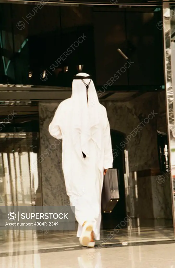 An Arab in traditional dress enters a commercial building.