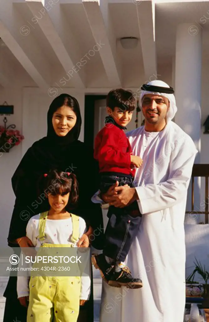 An Arab family stands outside their house and pose in front of the camera.