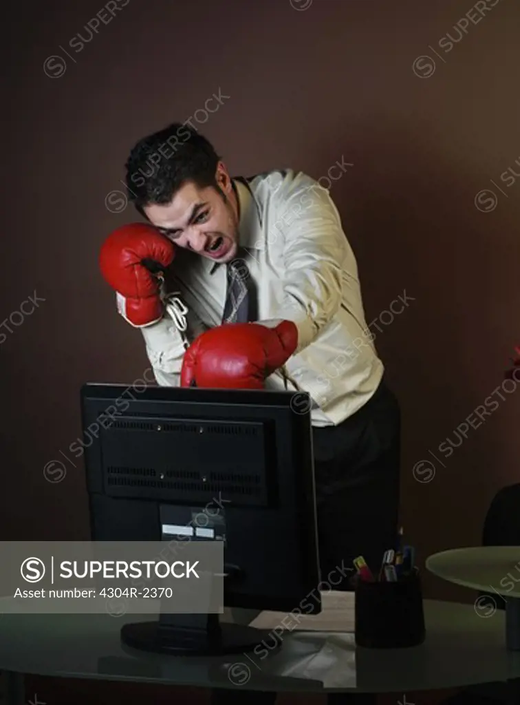 Young Businessman with boxing gloves attacking computer