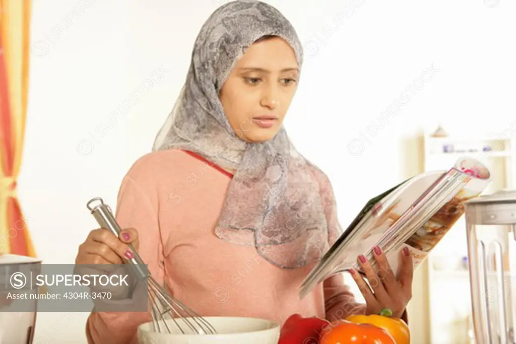 Arab lady cooking referring to a cookbook