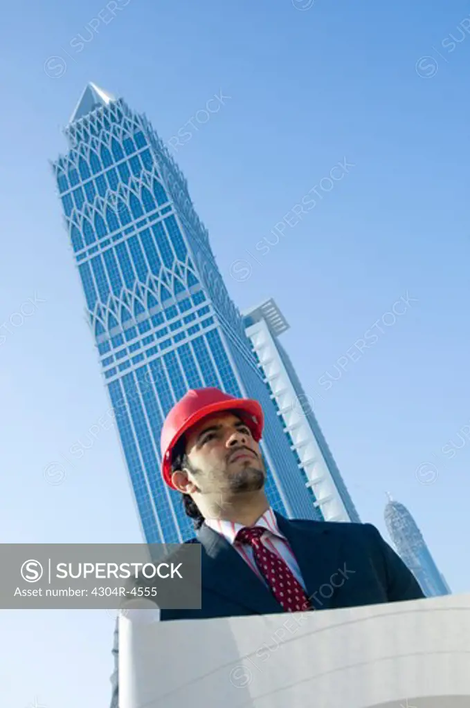 Young man wearing a red hard hat outdoors with skyscrapers in the background