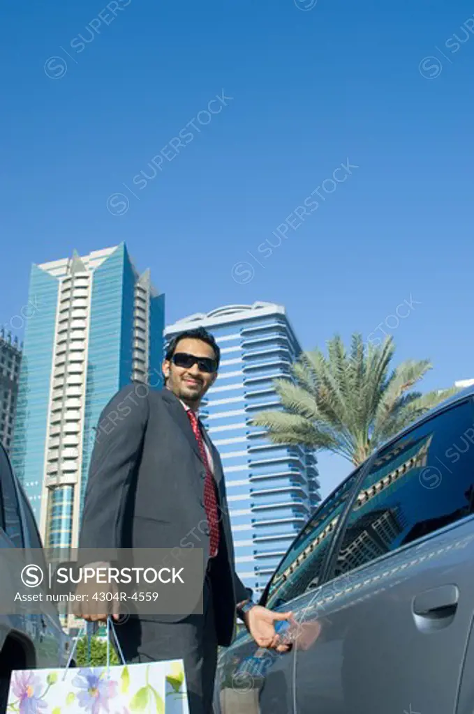 Young man with shopping bags near his car, outdoors with skyscrapers in the background