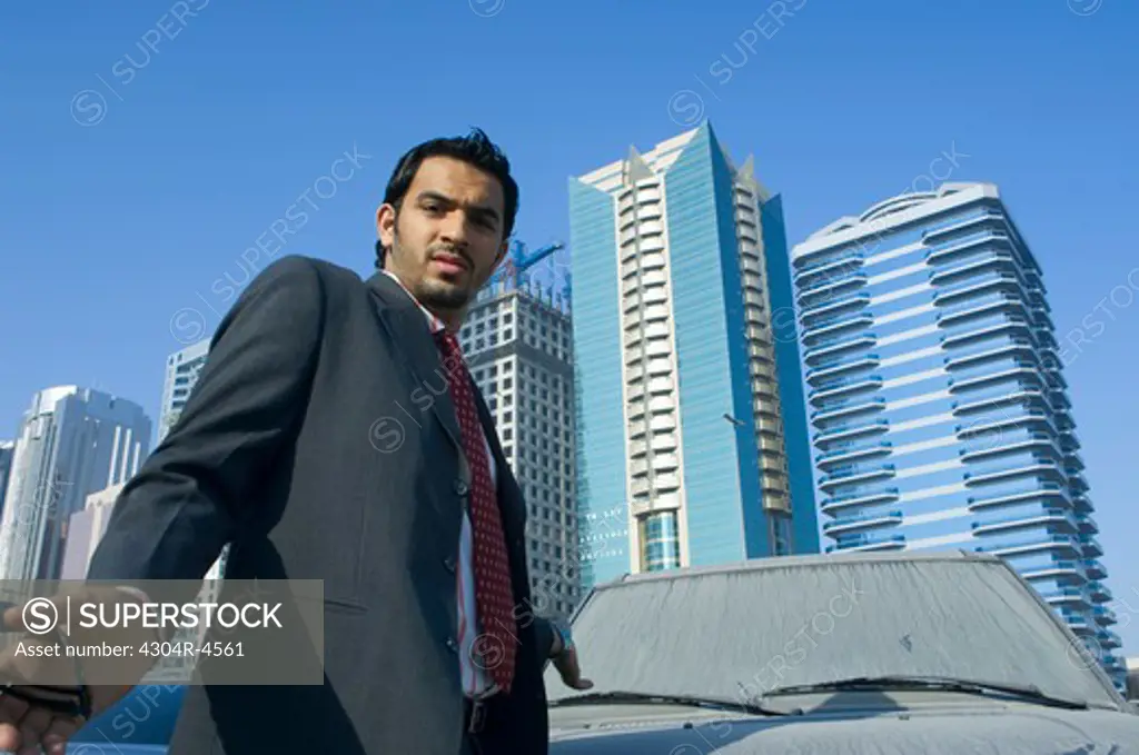 Young man pointing at a dirty car, outdoors with skyscrapers in the background