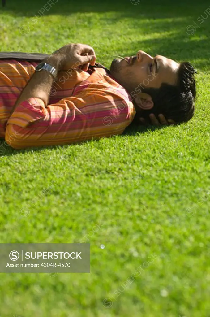 Young businessman lying on green grass relaxing