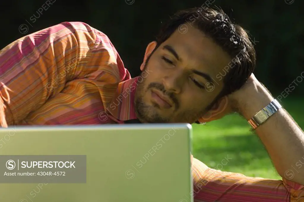 Young businessman lying on green grass & working on computer