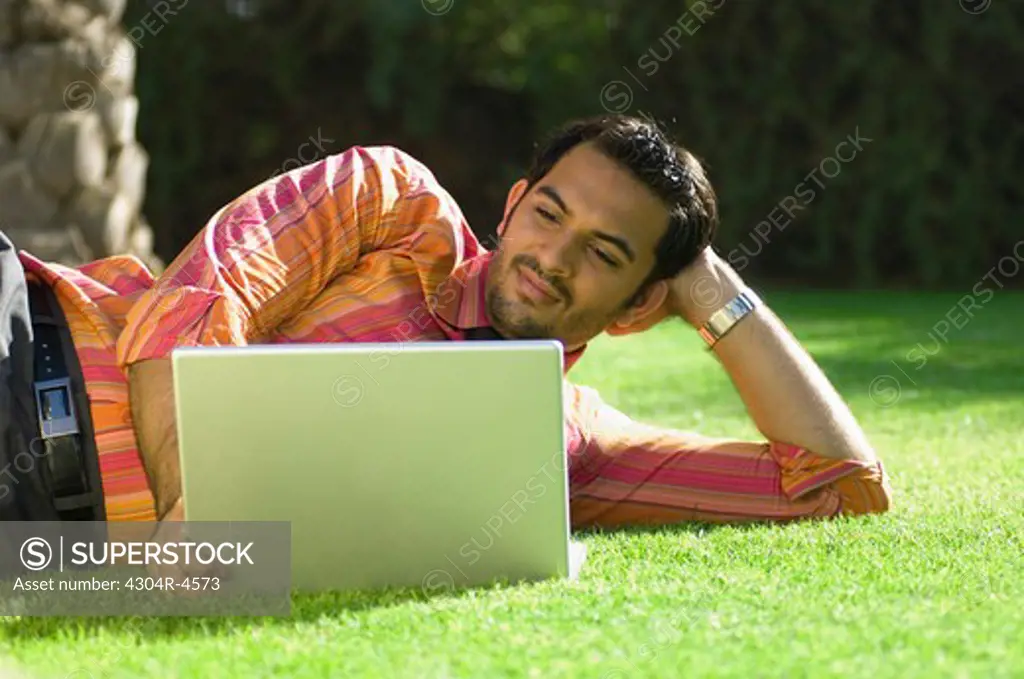 Young businessman lying on green grass & working on computer