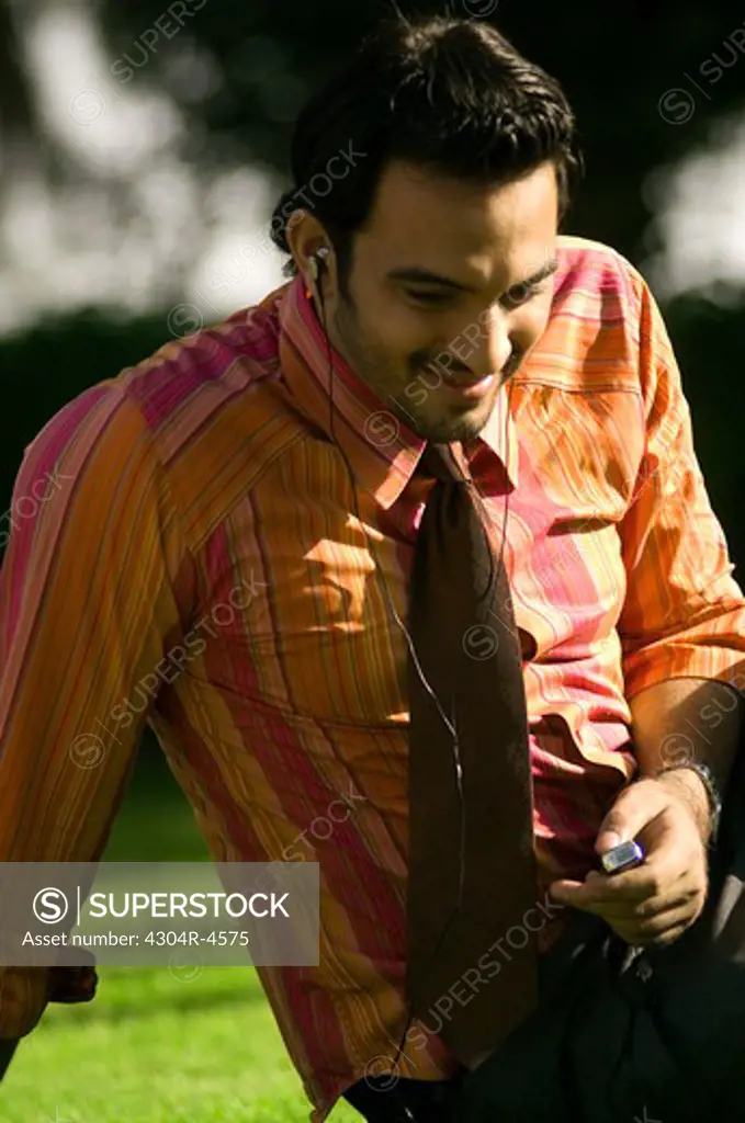 Young businessman sitting on green grass & listening to music