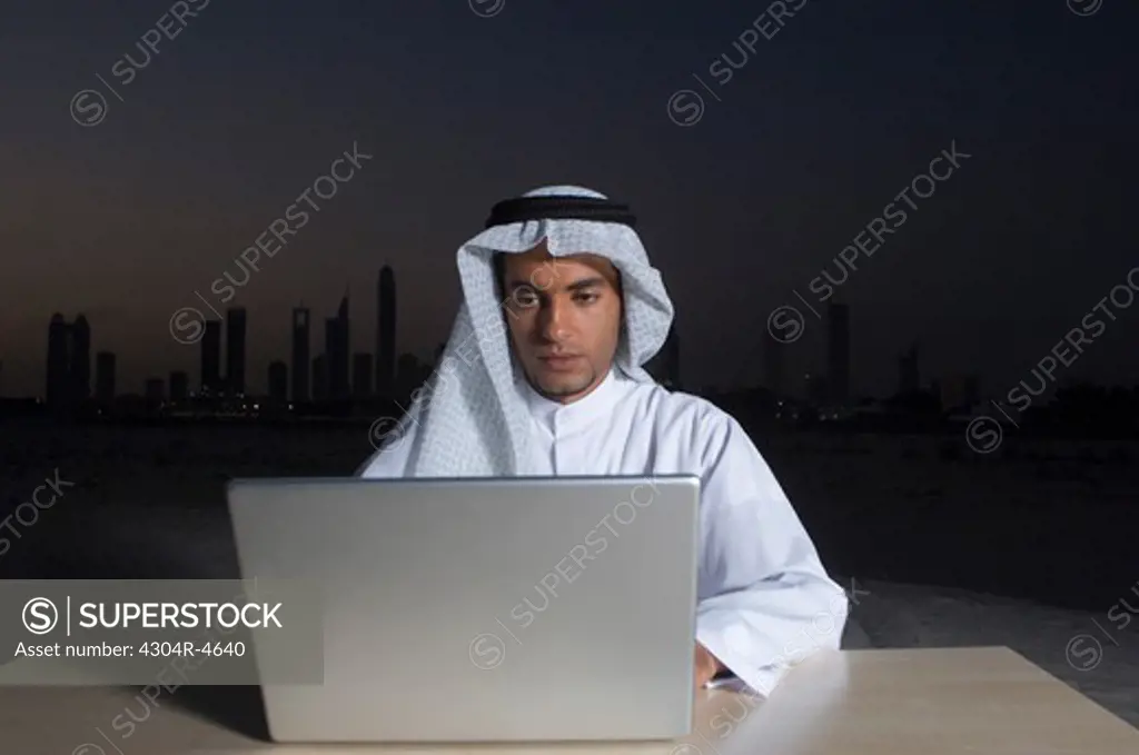 Young Arab man sitting at a desk - office with Dubai City in the background