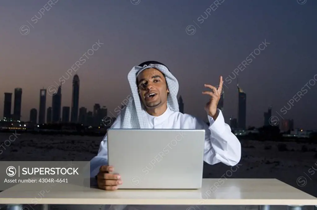 Young Arab man sitting at a desk - office with Dubai City in the background