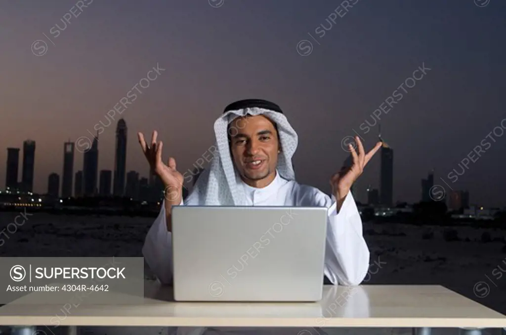 Young Arab man sitting at a desk - office with Dubai City in the background