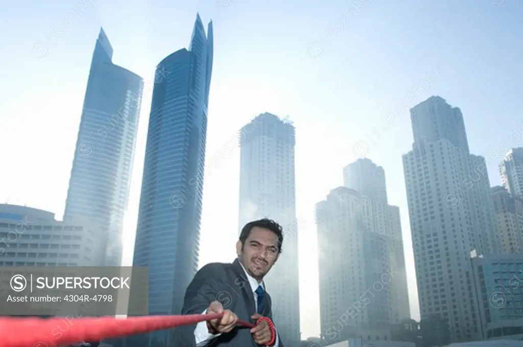 Businessman tugging rope, Towers seen through the mist in the background