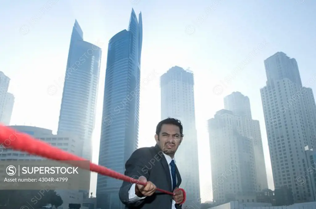 Businessman tugging rope, Towers seen through the mist in the background