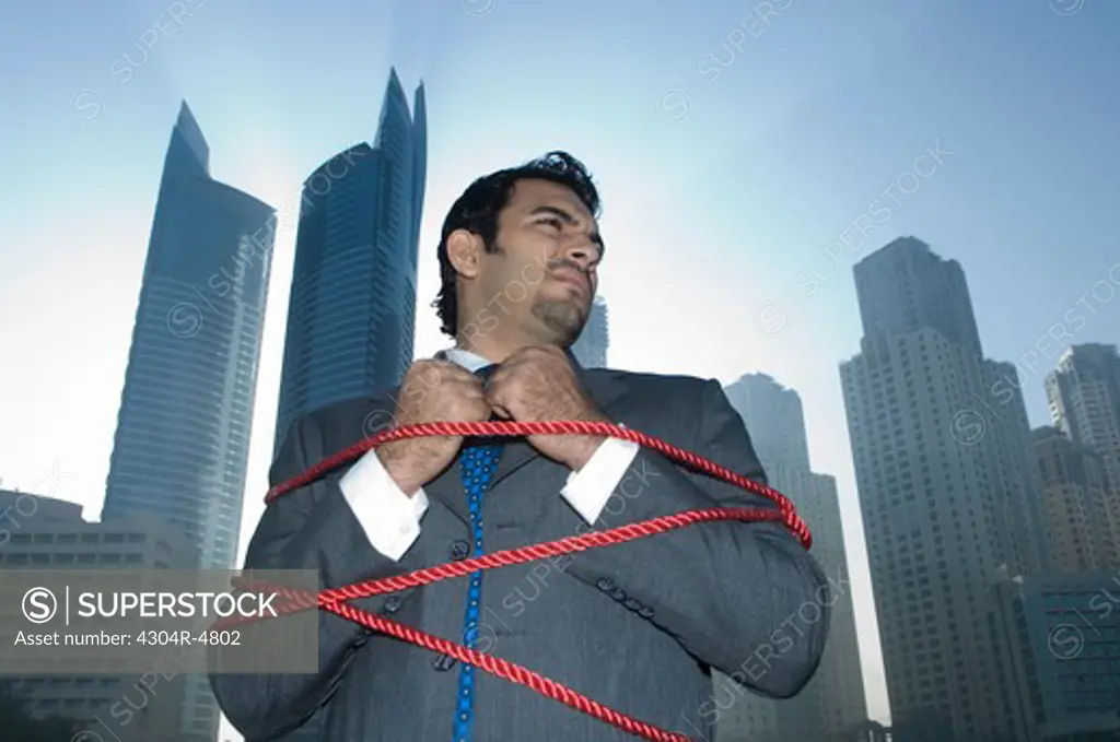 Businessman tied with rope, towers seen through the mist in the background