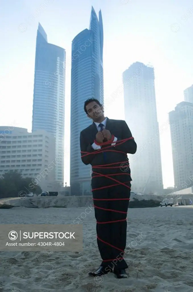 Businessman tied with rope, towers seen through the mist in the background