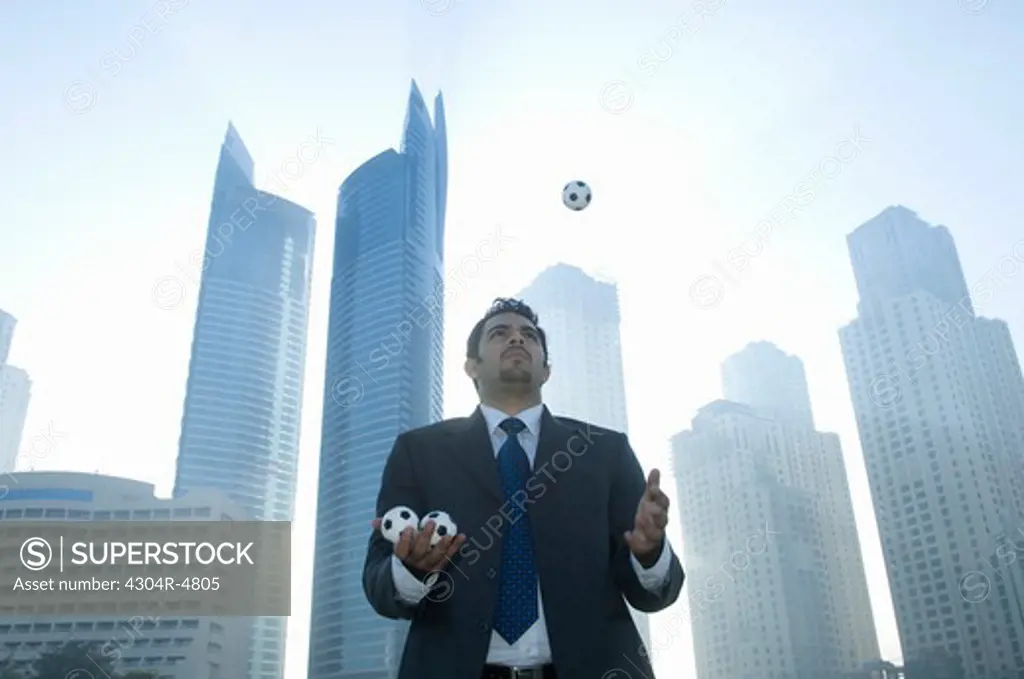 Businessman juggling, towers seen through the mist in the background
