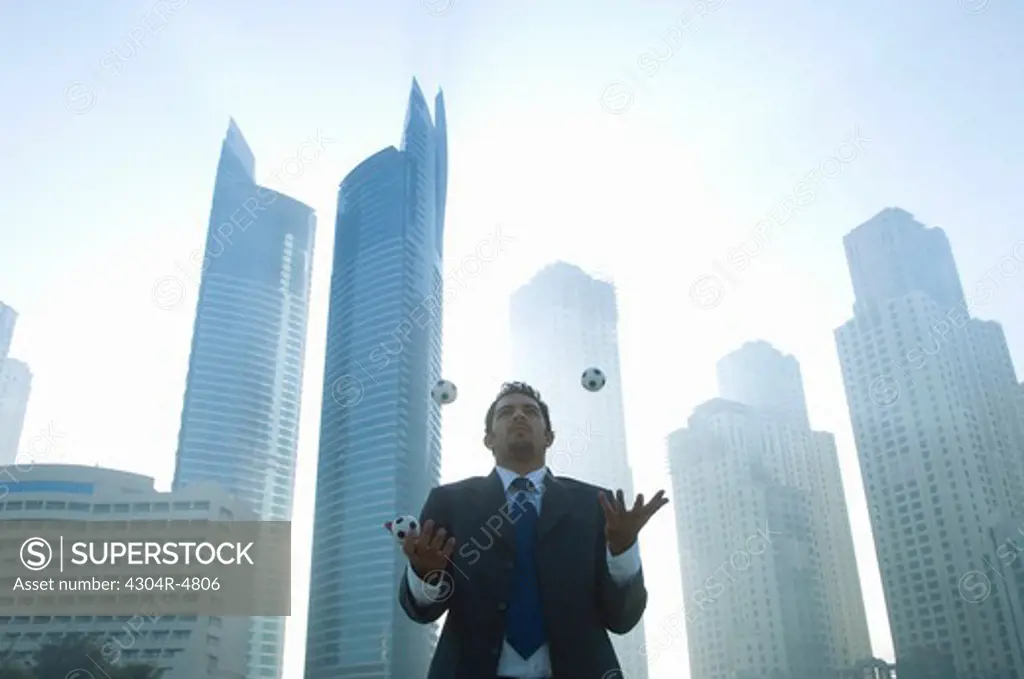 Businessman juggling, towers seen through the mist in the background