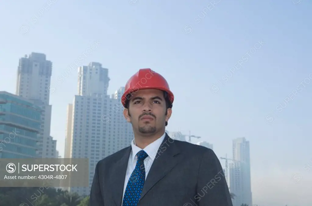 Businessman wearing hard hat, towers seen through the mist in the background