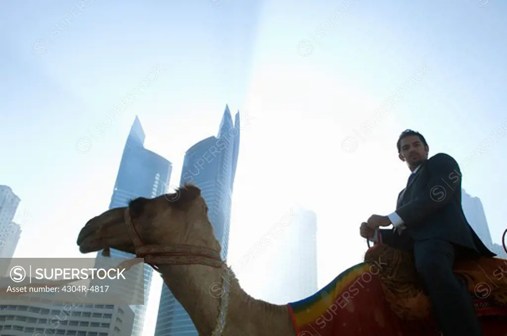Businessman sitting on camel, towers seen through the mist in the background