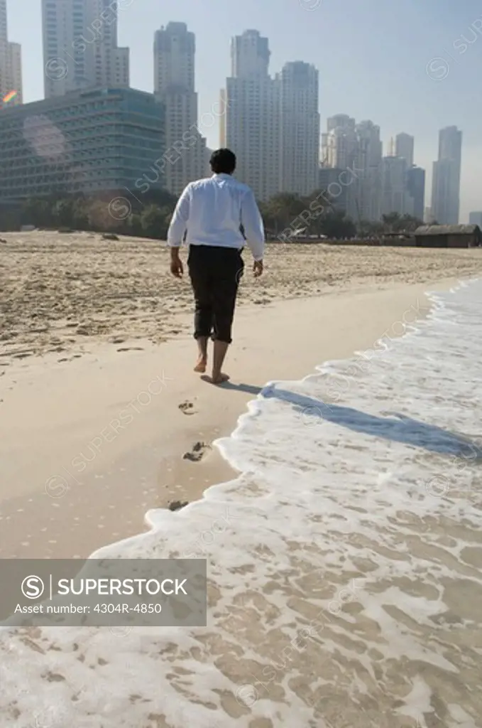 Businessman walking on the beach in formal wear, towers seen in the background