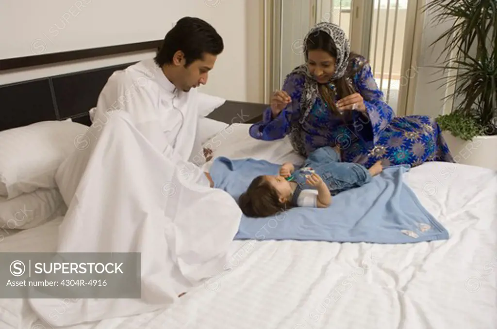 Parents sitting on the bed in the bedroom playing with baby