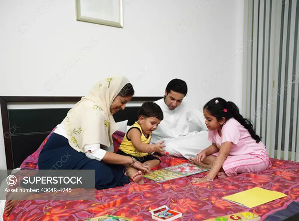 Family of four playing a board game on the bed