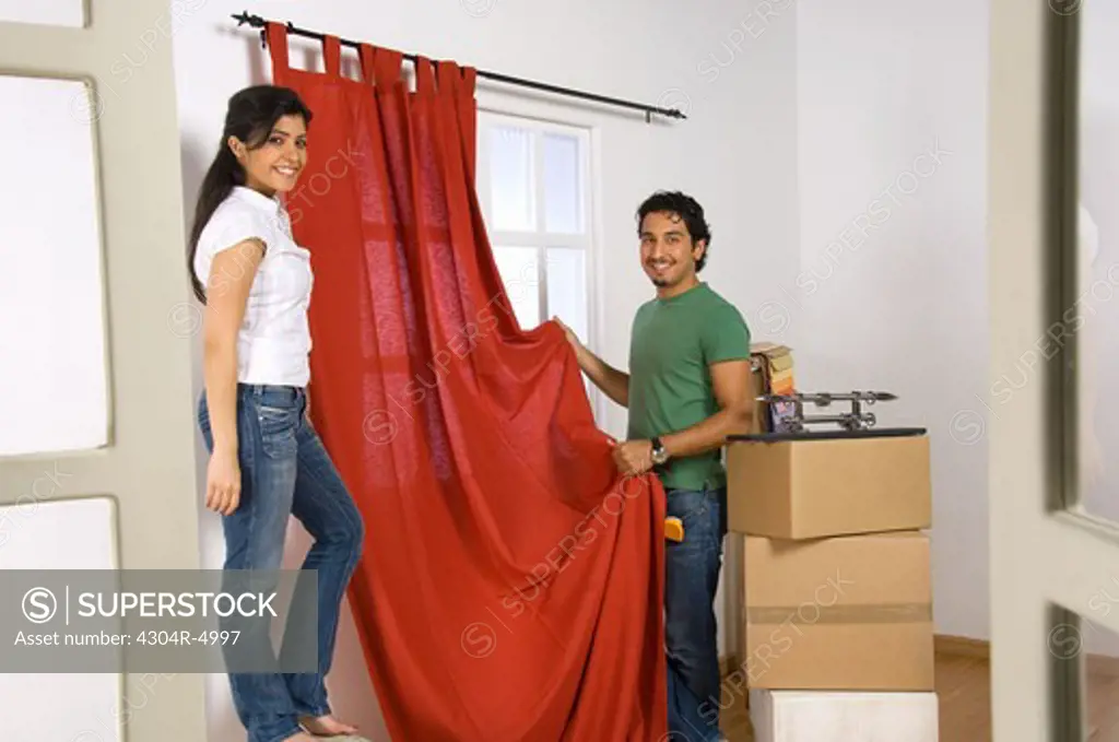 Young couple fixing the curtain on moving into a new home