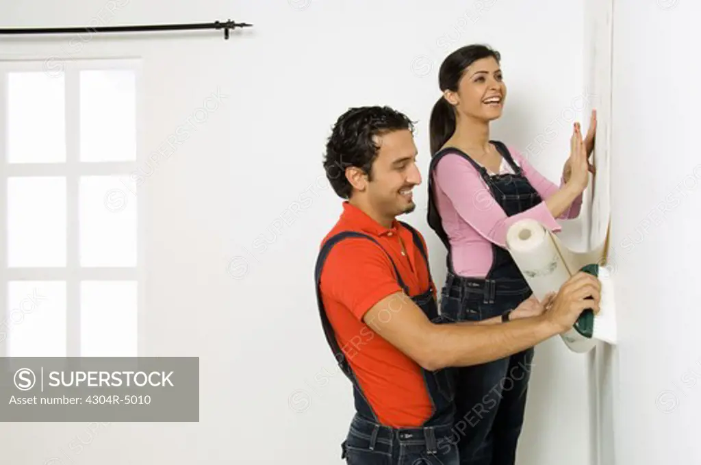 Young couple fixing wall paper