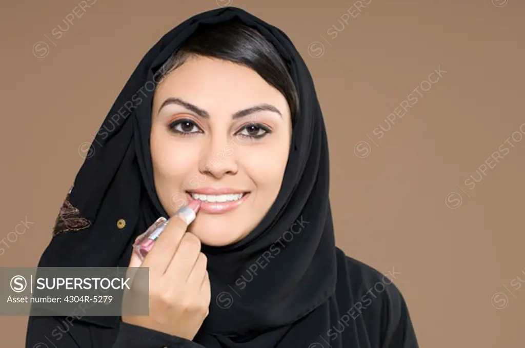 Young woman applying lipstick, smiling, portrait