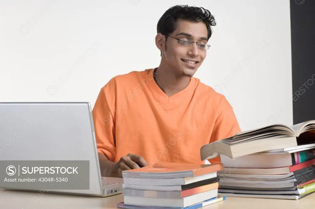 Young man with laptop reading book