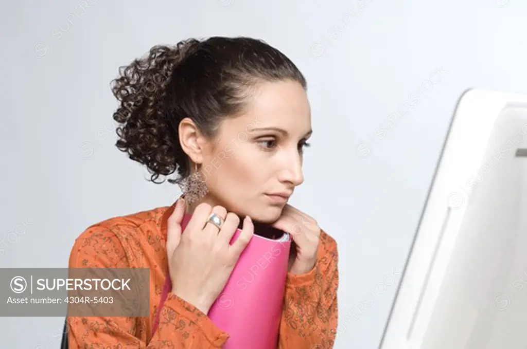 Young woman sitting by computer, holding book
