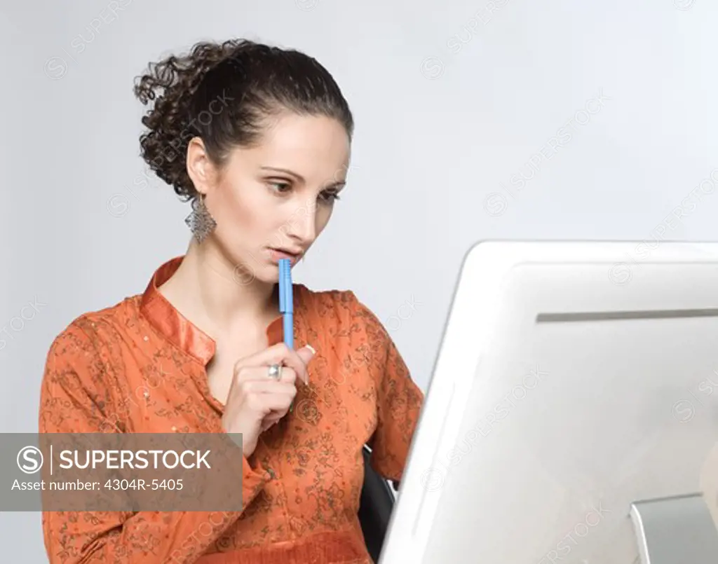 Young woman sitting by computer, holding pen