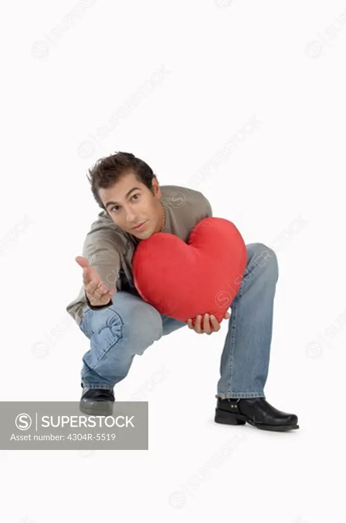 Young man holding heart-shaped cushion, portrait