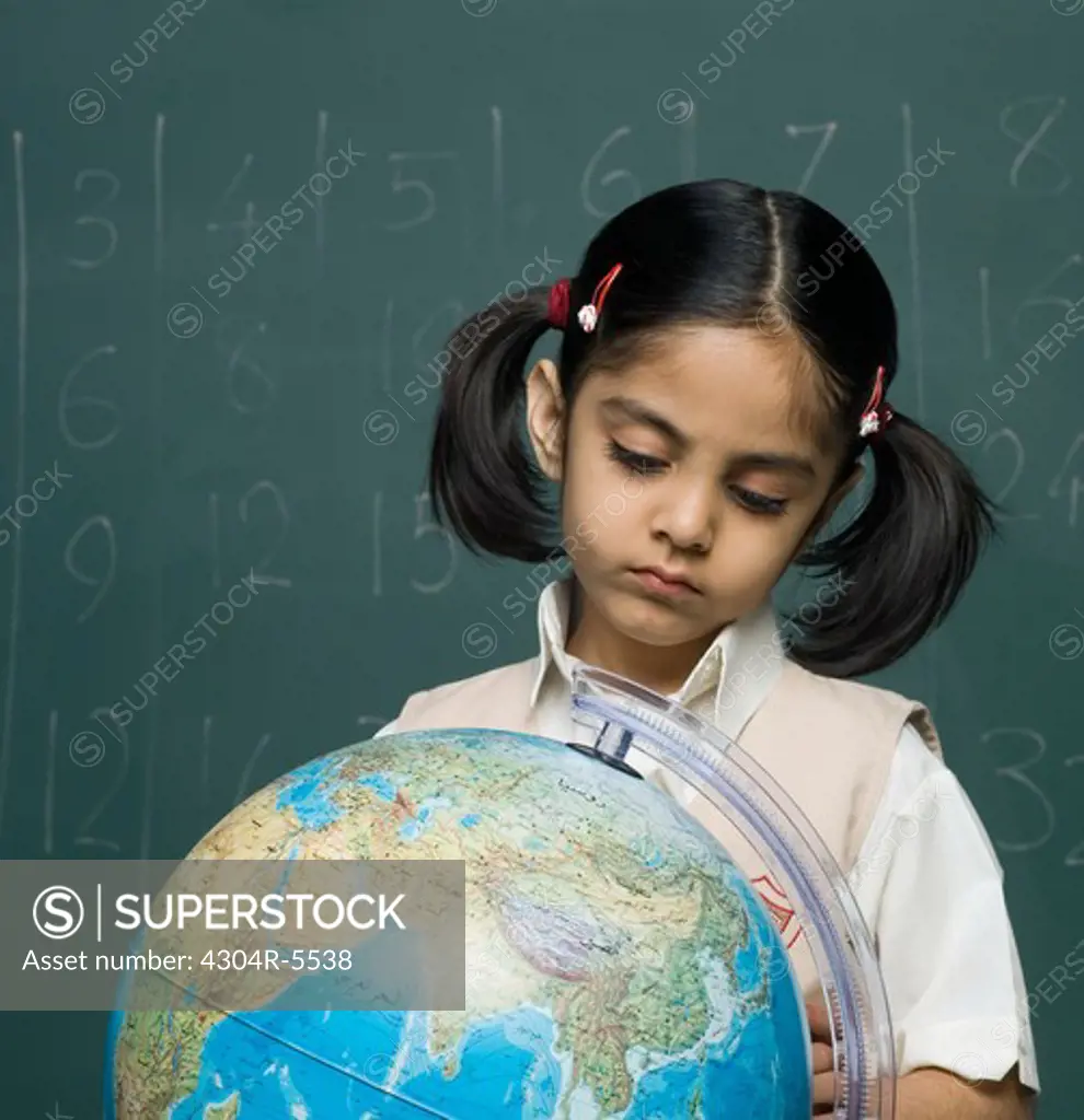 Girl (6-7) in classroom looking at globe